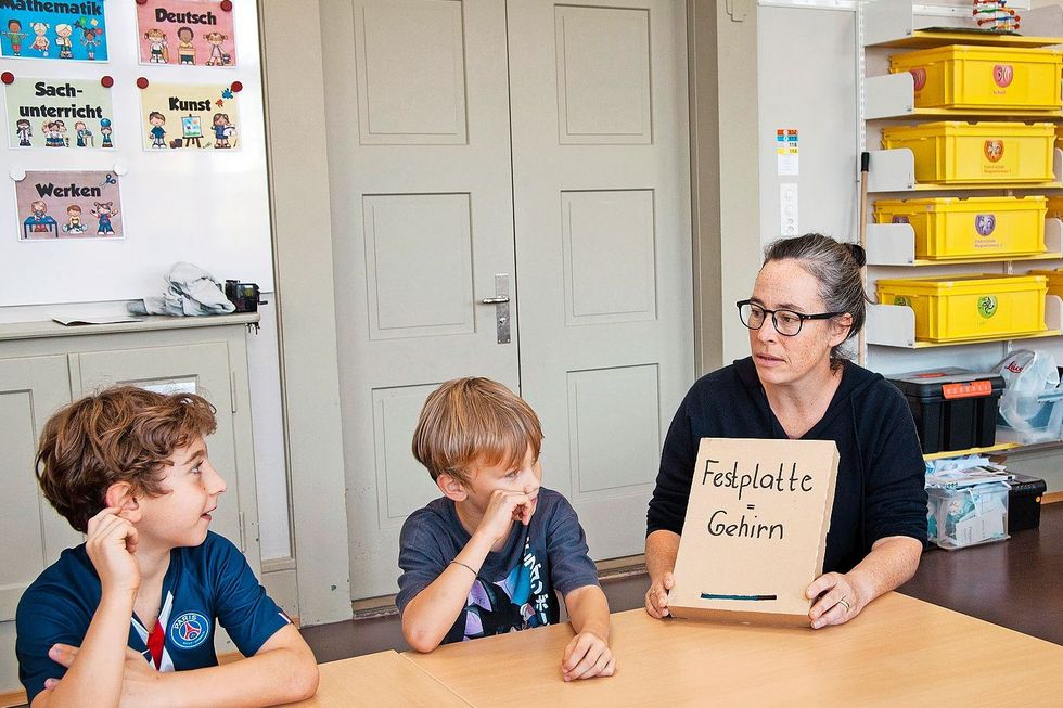 Primarschullehrerin Sara Cortellini zeigt einer Gruppe von Kindern einen Karton mit der Aufschrift "Festplatte". In diesem Karton befinden sich Karten mit Begriffen aus der digitalen Welt, die im Unterricht erklärt werden. Fotos: Roger Wehrli