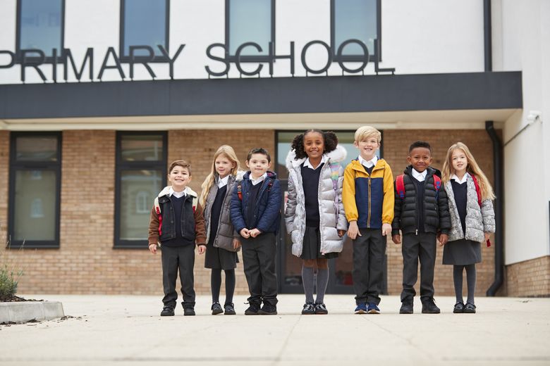 Primarschulkinder in Schuluniformen stehen vor der Schule. 