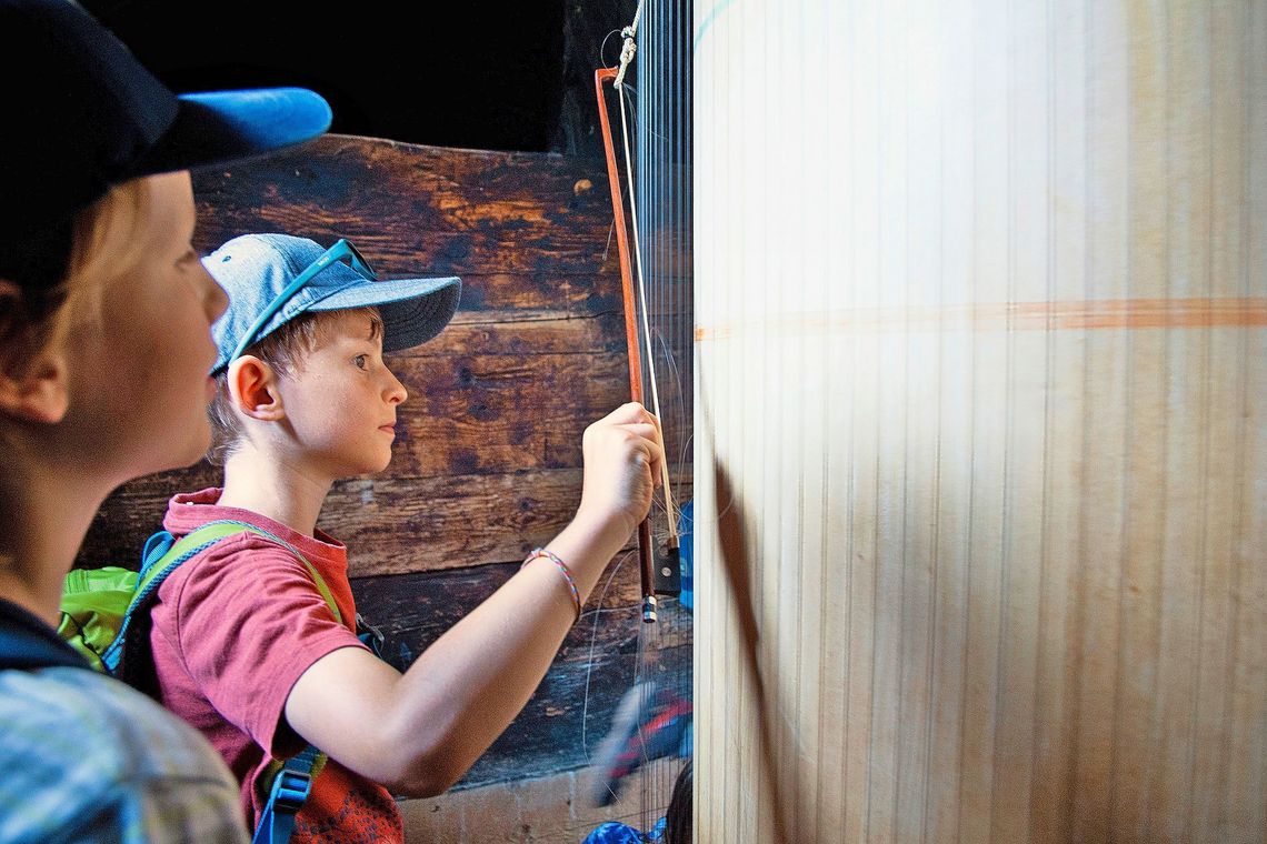 Ein Junge streicht mit einem Geigenbogen über ein grosses, saitenbespanntes Objekt.