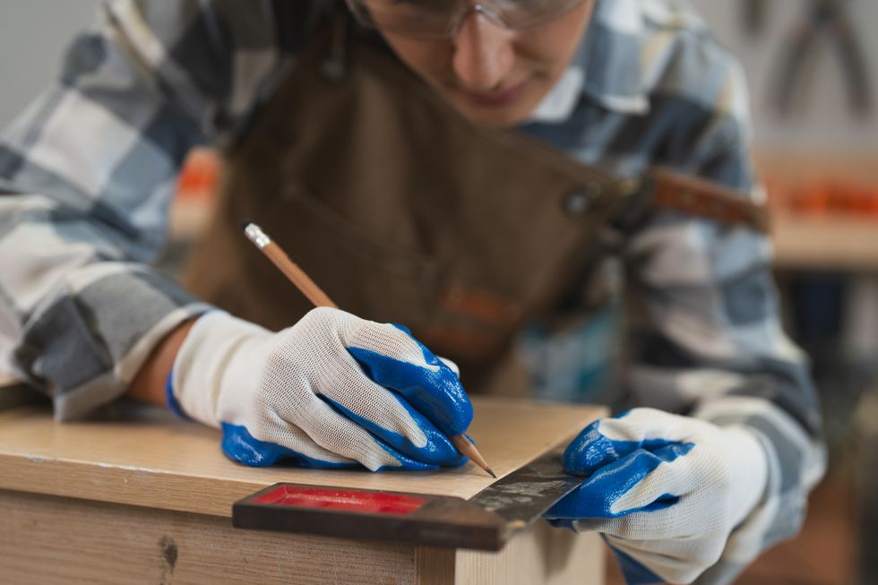 Hände messen die Länge einer Holzplanke.