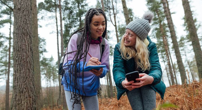 Zwei Mädchen sind mit dem Handy im Wald unterwegs.