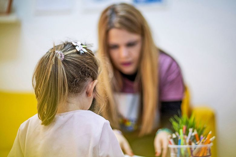 Ein Kind sitzt am Tisch vis-à-vis ihrer Lehrerin, die ihr etwas zeigt.