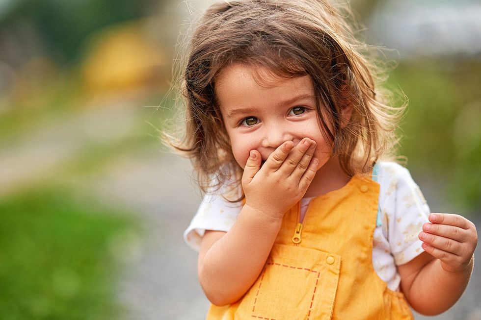 1172643701 Kind hält sich den Mund zu.