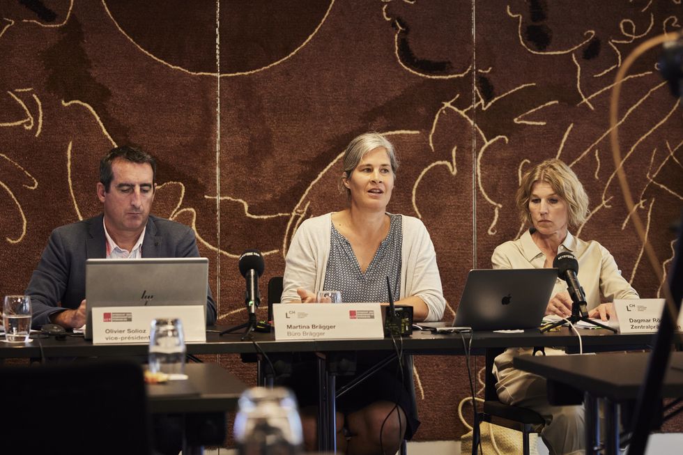 Olivier Solioz, Martina Brägger und Dagmar Rösler sitzen an Pulten. Eine Kamera ist auf sie gerichtet.