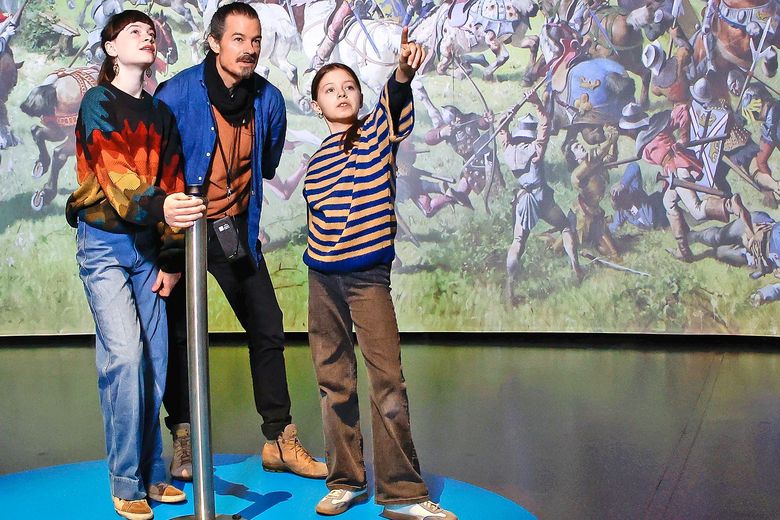 Ein Mann und zwei Kinder stehen vor dem grossen Panoramabild der Schlacht bei Murten.