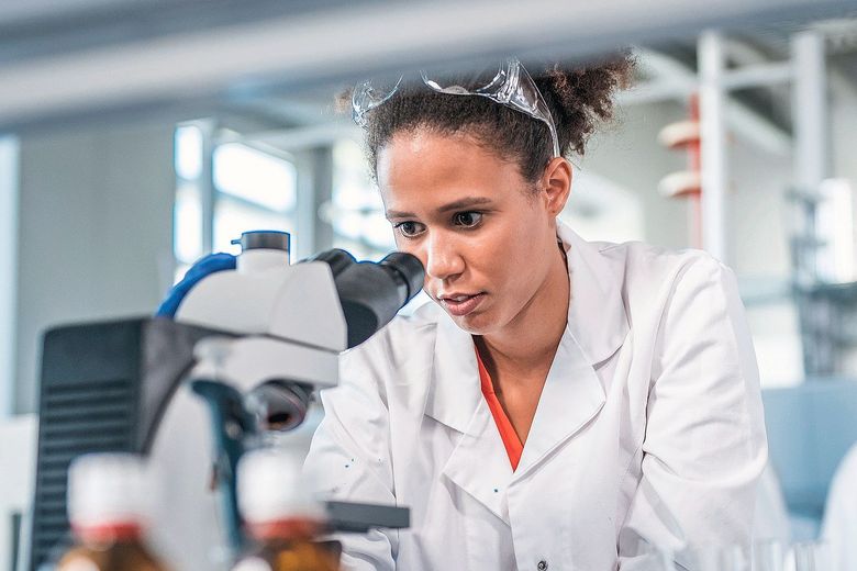 Eine junge Frau schaut in ein Mikroskop.