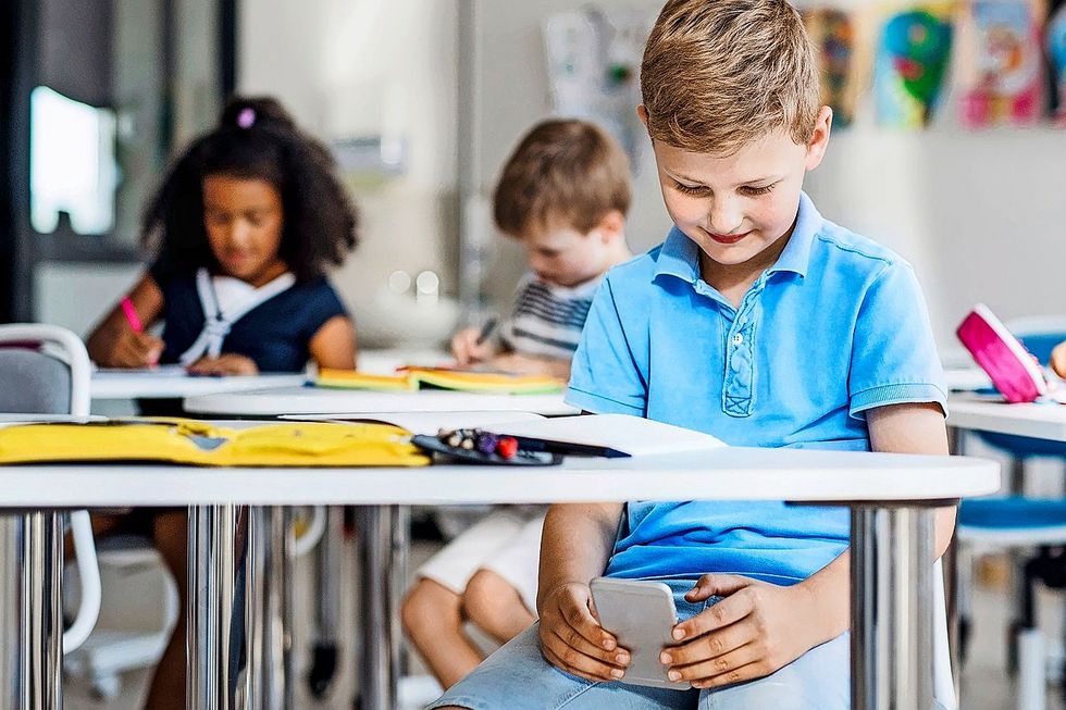 Kind schaut auf sein Smartphone während des Unterrichts.