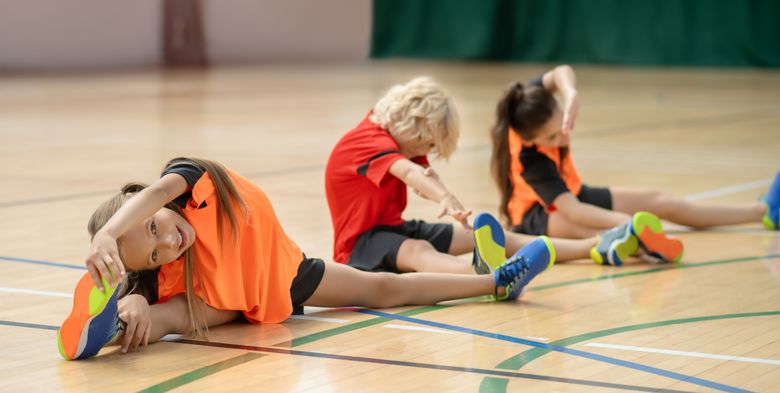Kinder dehnen in einer Turnhalle Beine und Arme