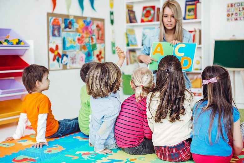 Sprachförderung Eine Gruppe von Kindern sitzt auf dem Boden und hört einer Lehrerin zu, die das Alphabet erklärt. Foto: iStock/svedikd