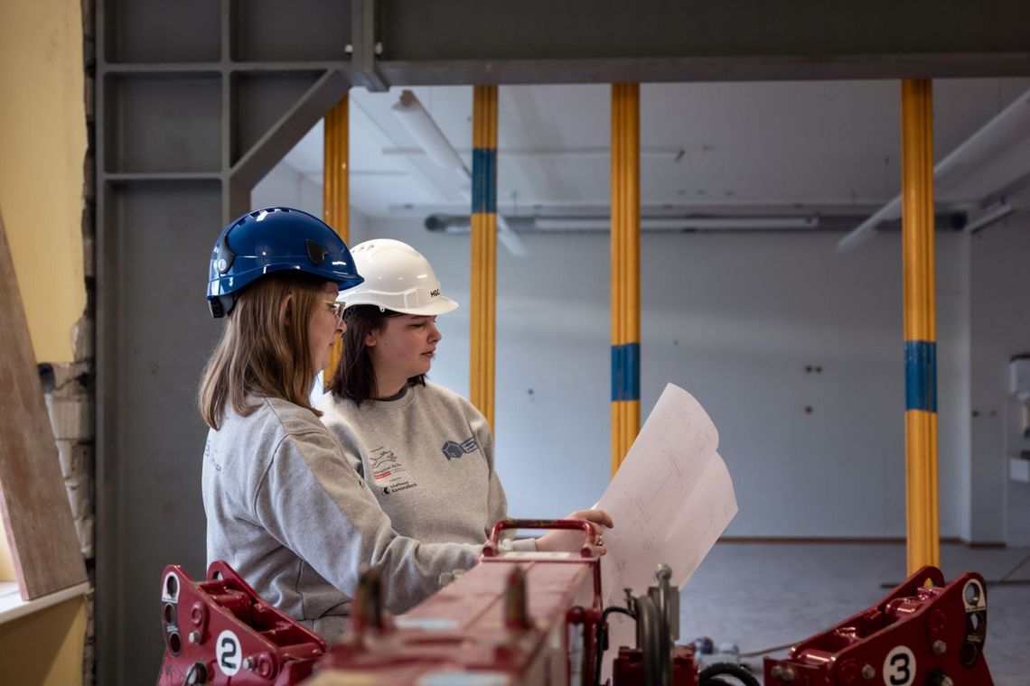 zwei junge Frauen mit Bauhelmen schauen auf der Baustelle einen Plan an