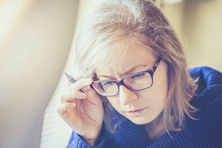 Erwachsene Frau greift sich beim Lesen an die Brille.