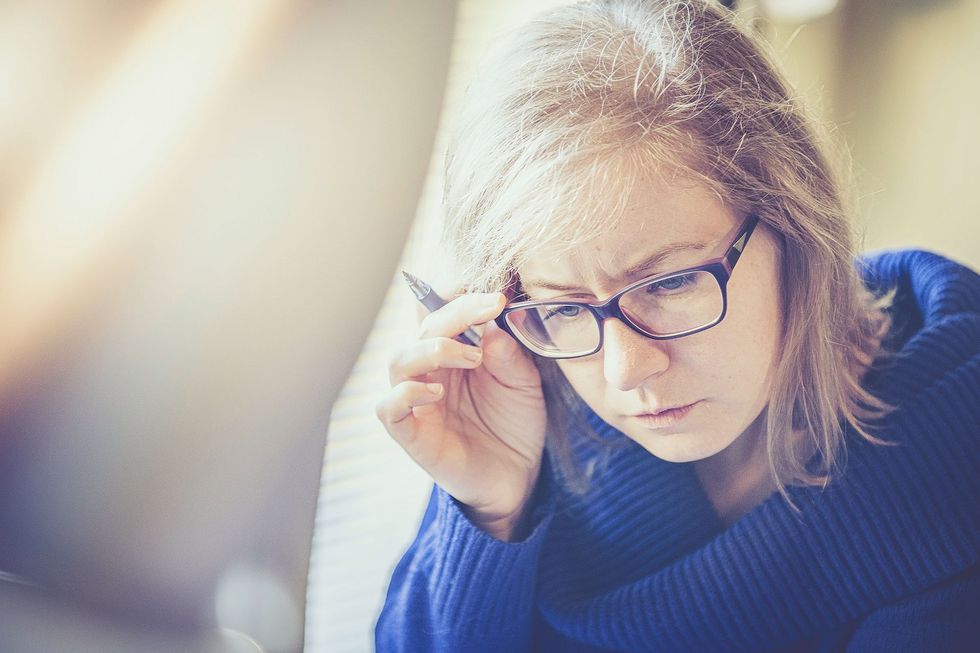 Erwachsene Frau greift sich beim Lesen an die Brille.