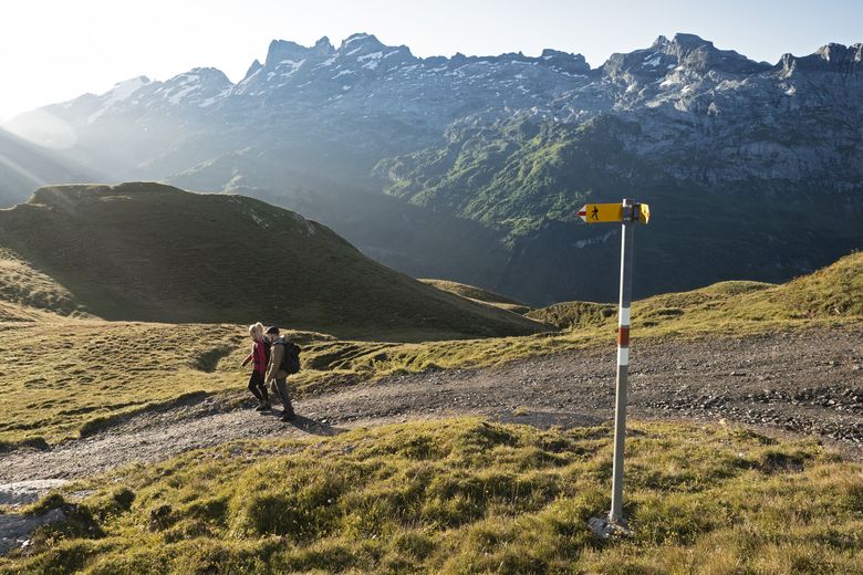 Zwei Personen mit Rucksäcken auf einem Wanderweg inmitten einer Bergkulisse