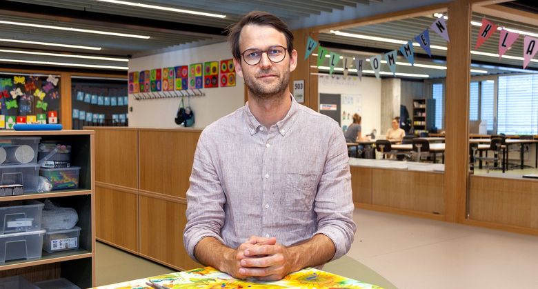 Mann steht vor Klassenzimmer mit grossen Fenstern.