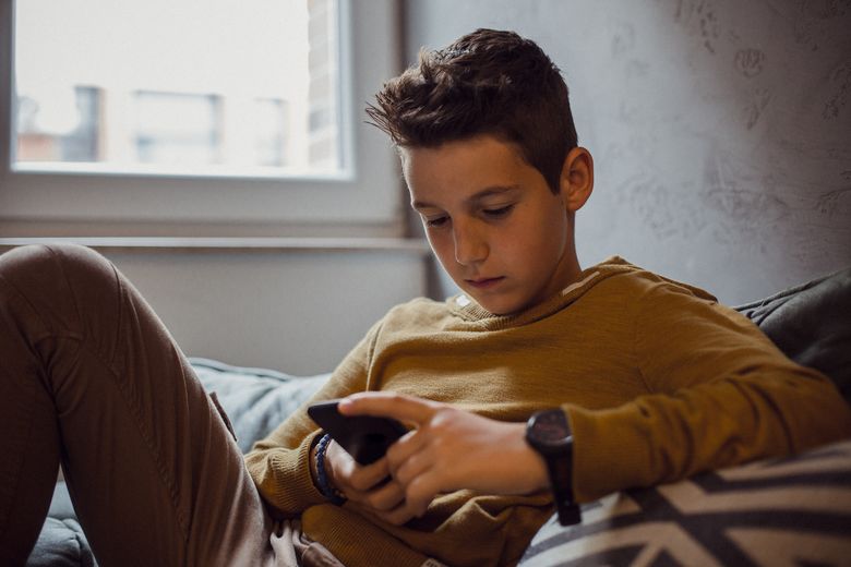 Teenage Boy Relaxing in his Bedroom Teenager liest am Handy.