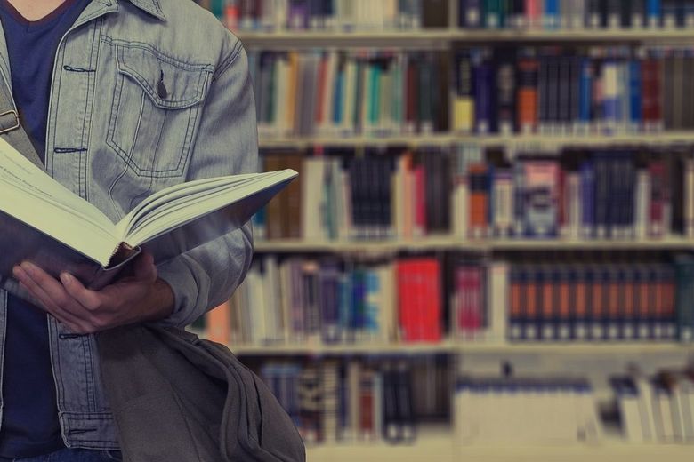 Ein Student steht mit einem Buch in den Händen in einer Bibliothek.