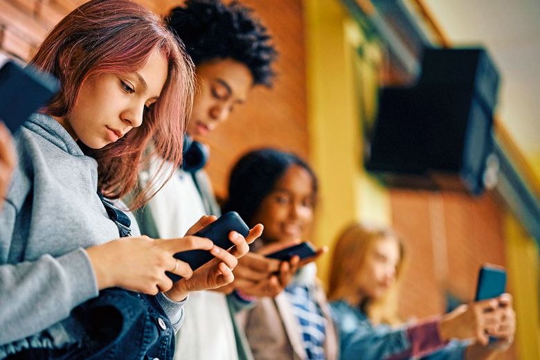Schüerinnen und Schüler schauen auf ihr Handy.