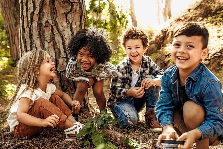 Eine Gruppe Kinder sitzt lachend im Wald.