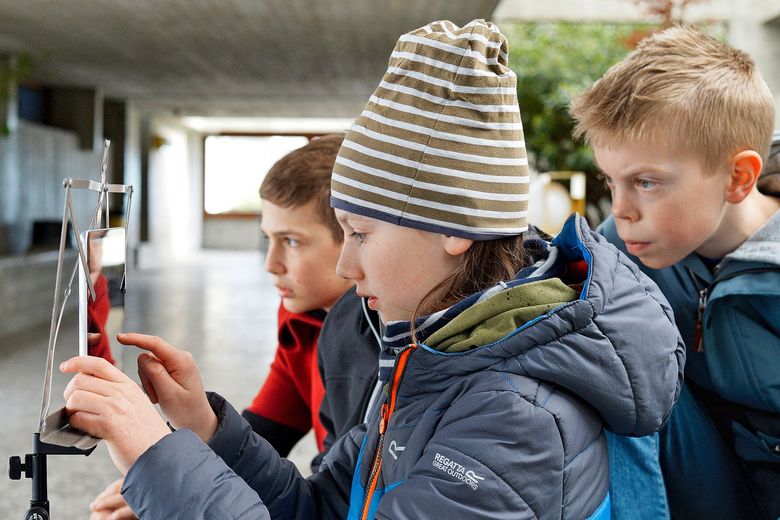 Drei Kinder sind draussen und schauen auf ein Tablet.