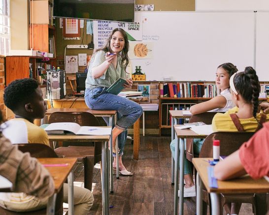 Frau sitz auf einem Tisch vor einer Schulklasse