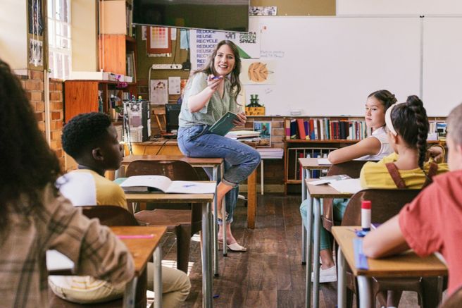Frau sitz auf einem Tisch vor einer Schulklasse