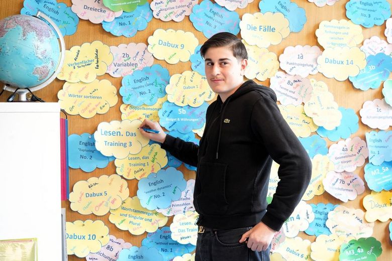 Junge steht vor einer Wand, die mit Wolken aus Papier.