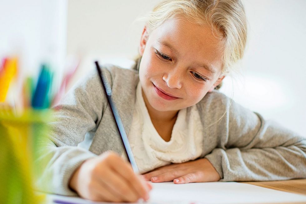 Ein Kind sitzt an einem Tisch und schreibt oder zeichnet etwas auf ein Blatt Papier.