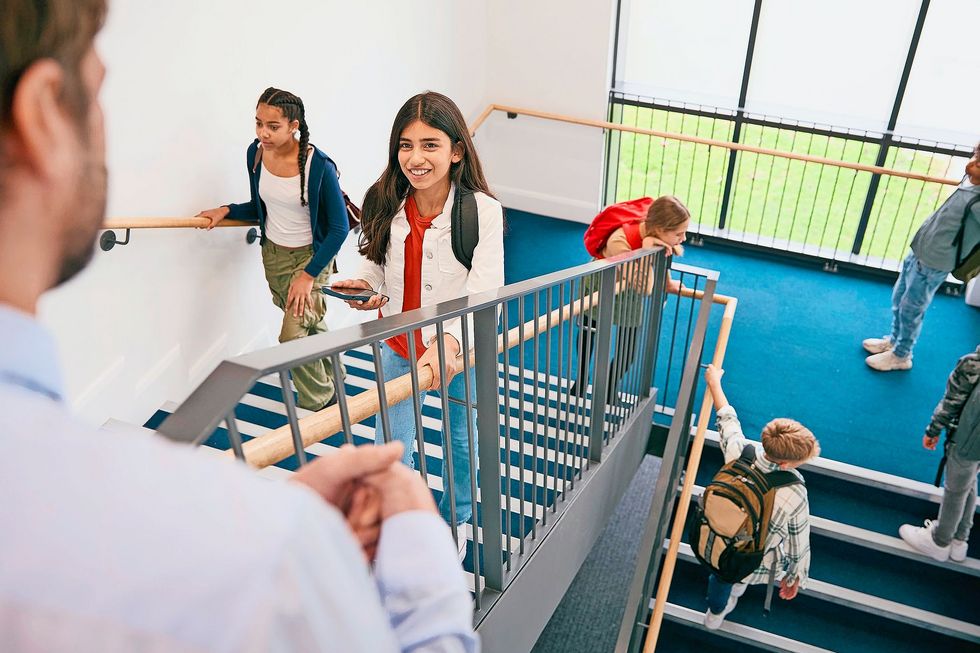 Teacher Looking Down On Group Of Secondary Or High School Pupils Inside School Building On Stairs