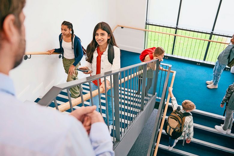 Teacher Looking Down On Group Of Secondary Or High School Pupils Inside School Building On Stairs