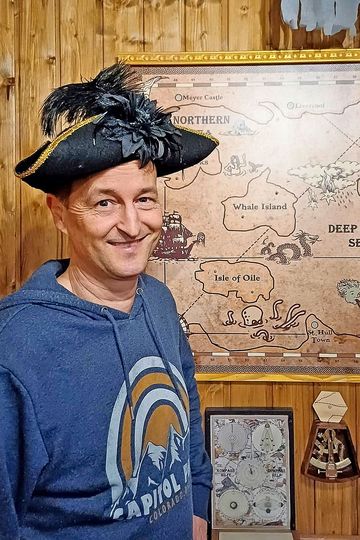 Ein Mann mit Piratenhut steht vor einer Schatzkarte. 
