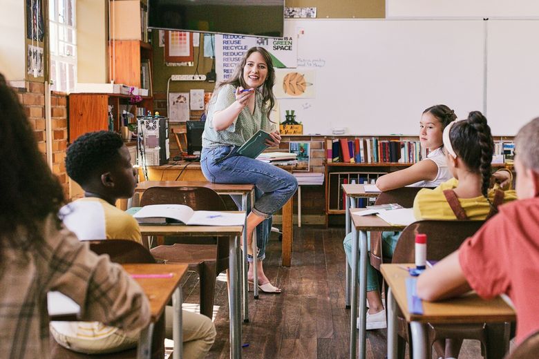 Eine Lehrerin sitzt vor ihrer Klasse auf einem Pult.