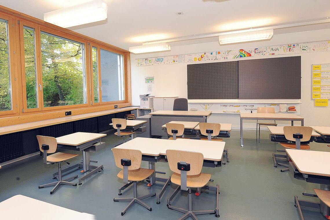 Schulzimmer mit Stühlen, Tischen und Wandtafel.