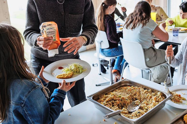 Reportage Tagesschule Prêles Betreuungsperson schöpft einem Kind an einem Mittagstisch Essen auf einen Teller.