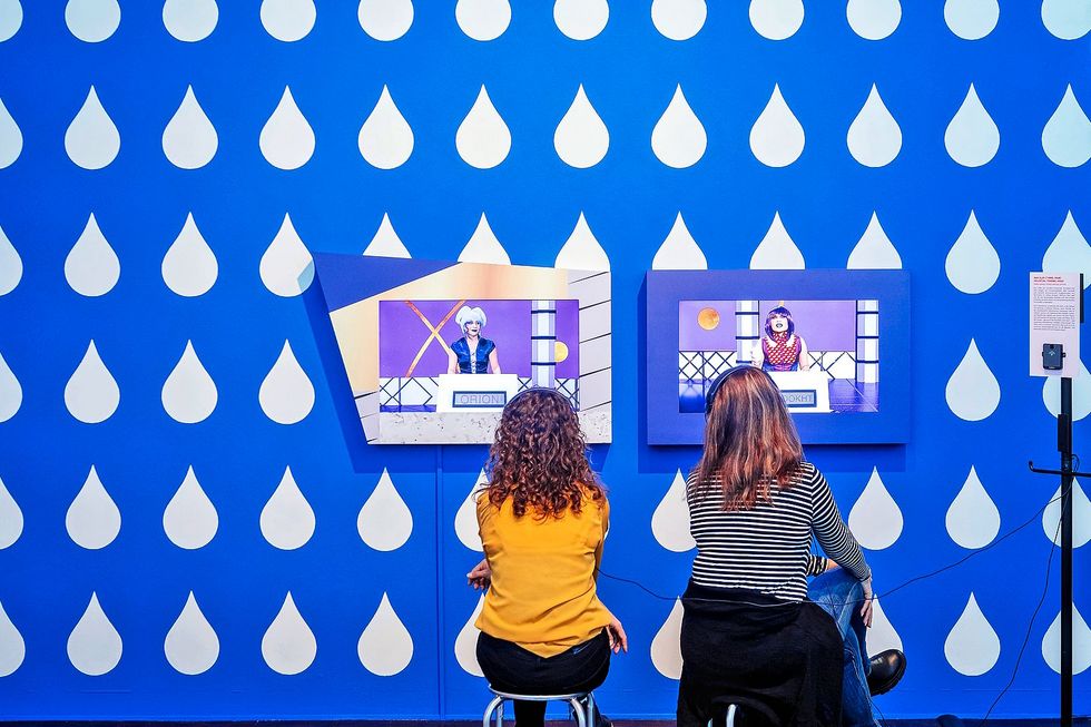 Macht Zwei Jugendliche Sitzen vor einer bunten Wand mit Bildschirmen.