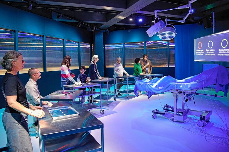 Ausstellungsbesucherinnen und -besucher stehen um einen violett beleuchteten Operationstisch.