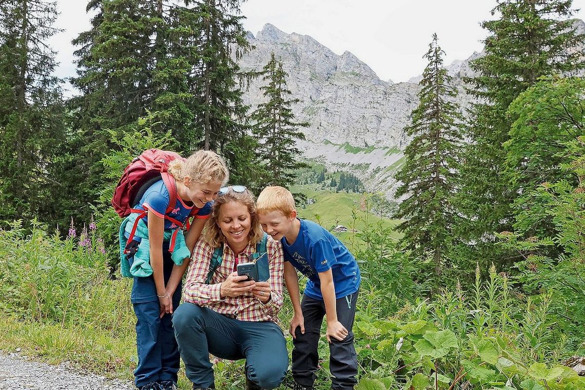 Eine Frau und zwei Kinder stehen auf dem Wanderweg und schauen interessiert in ein Handy.