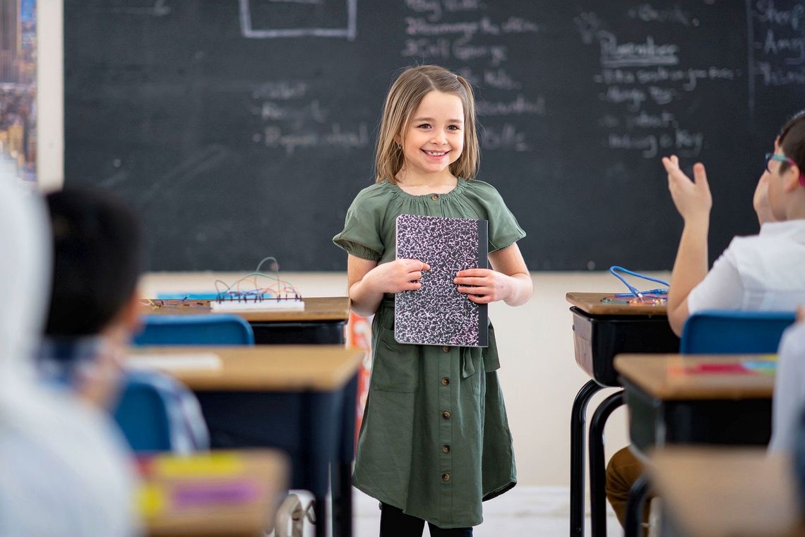 Ein Mädchen hält vor der Klasse einen Vortrag und lächelt.