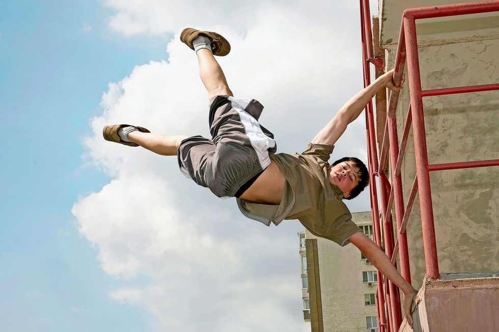 Ein Junge nutzt ein Geländer als Turngerät. Seine Beine sind in der Luft.