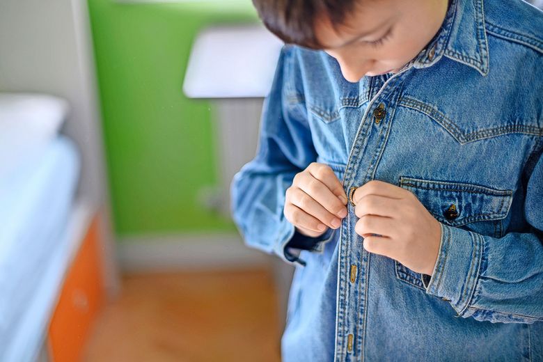 Ein Kind knüpft sich das Jeanshemd zu.