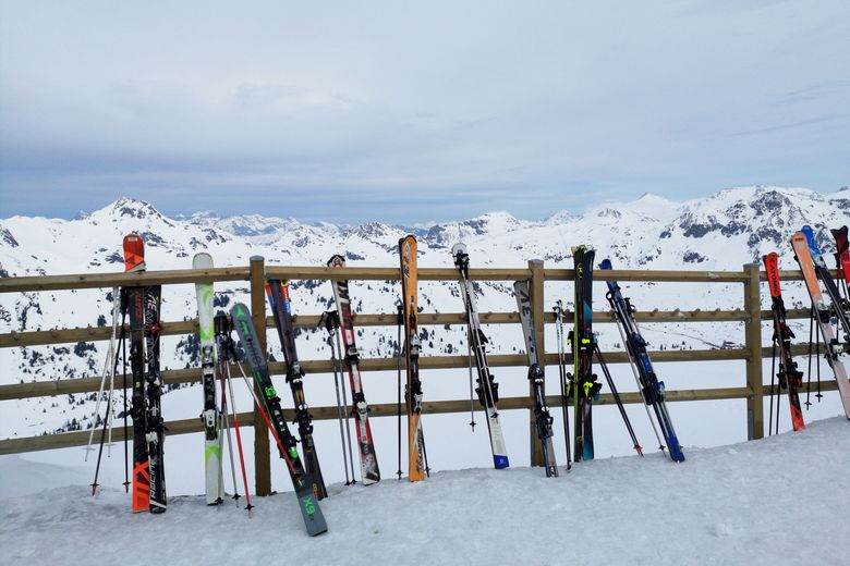 Skis und Stöcke lehnen an einem Holzzaun vor einem Bergpanorama.