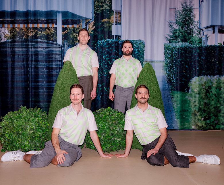Drei Männer in grauen Hosen und grünweiskarierten Poloshirts stehen auf einer Bühne.