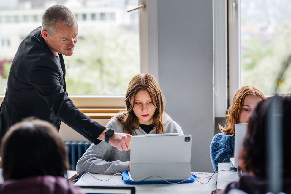 Lehrer instruiert eine Schülerin, die am Laptop sitzt.