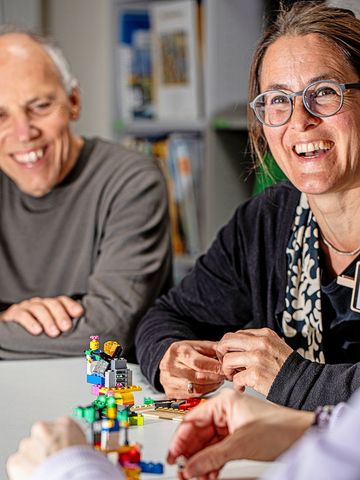 Eine Lehrerin und ein Lehrer sitzen am Tisch vor einem Legomodell.