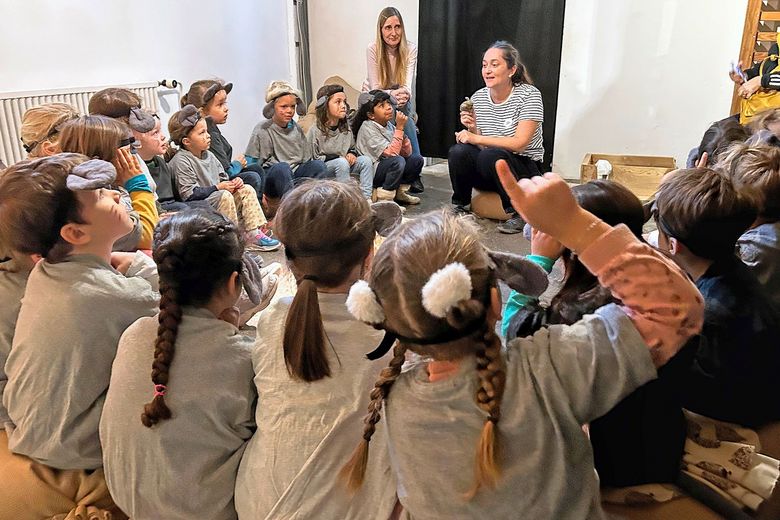 als Mäuse verkleidete Kinder sitzen in einem Halbkreis und lauschen, was eine Frau erzählt