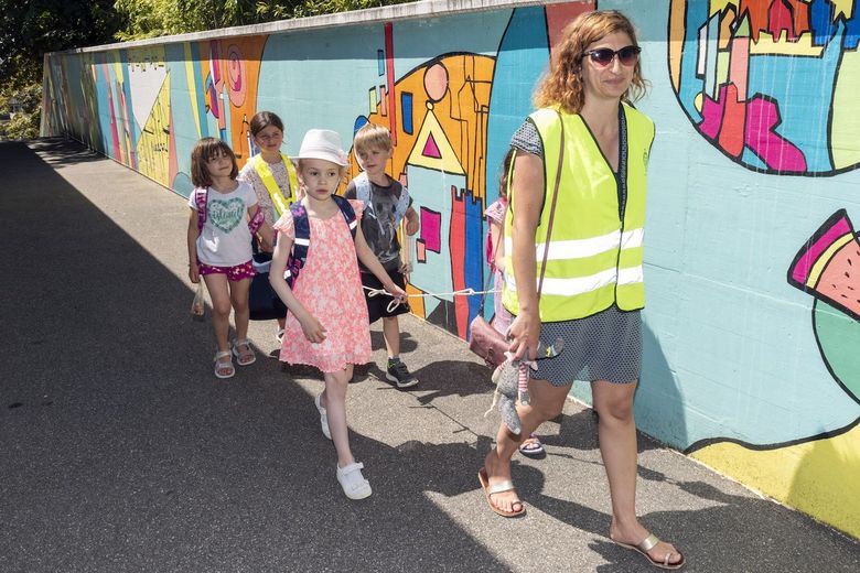 Mutter führt Schulkinder, die sich an einem Seil festhalten.