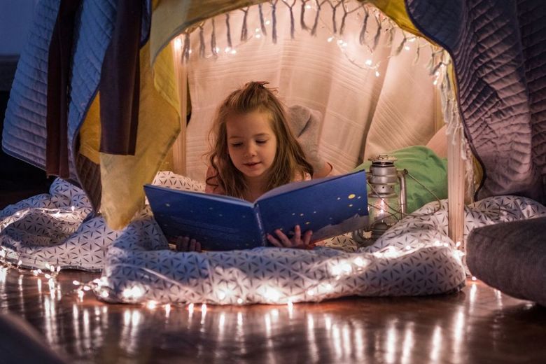 Ein Mädchen liegt in Höhle aus Tüchern und liest in einem grossen Buch.