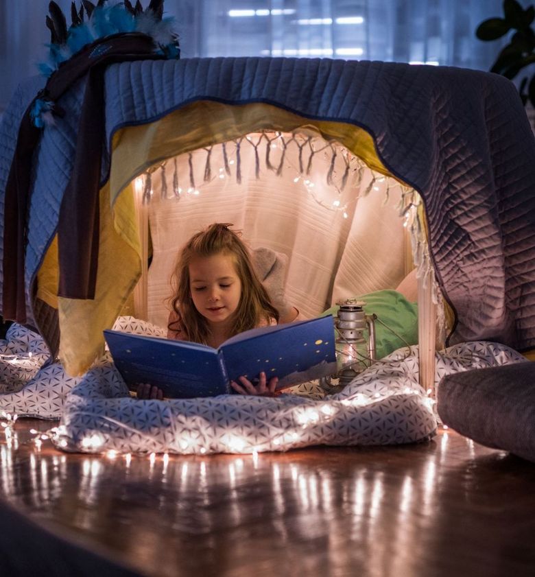 Ein Mädchen liegt in Höhle aus Tüchern und liest in einem grossen Buch.