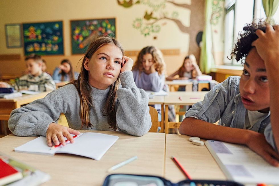 1792526146 Bored schoolgirl and her friends on a class in the classroom.