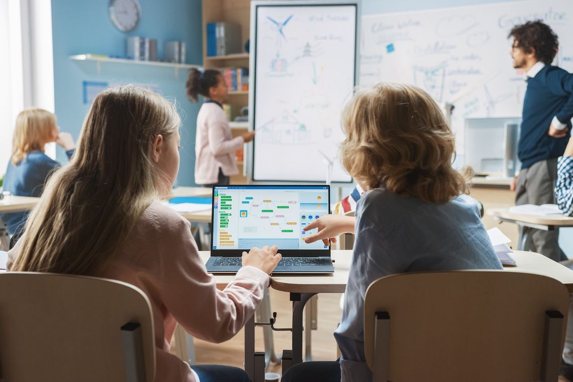 Zwei Schulkinder besprechen am Laptop ein Computerprogramm.