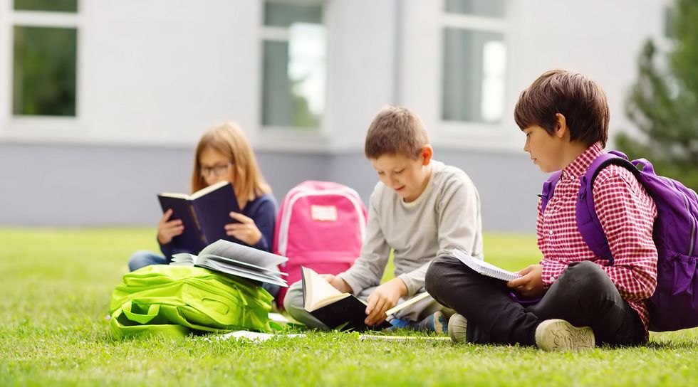 Schulkinder sitzen lesend auf der Schulwiese.